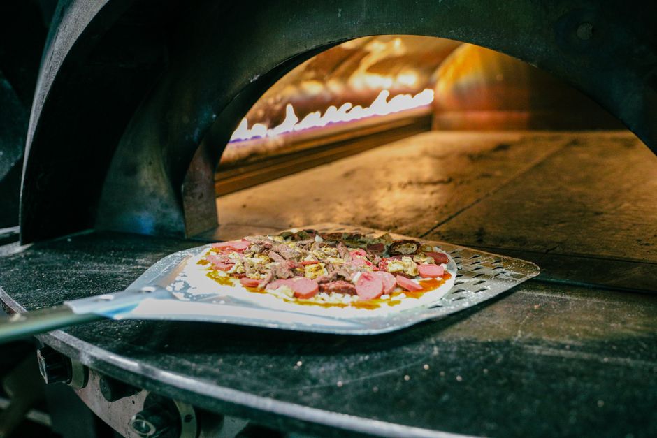 Pizzaiolo připravuje pizzu u rozpálené pece na dřevo